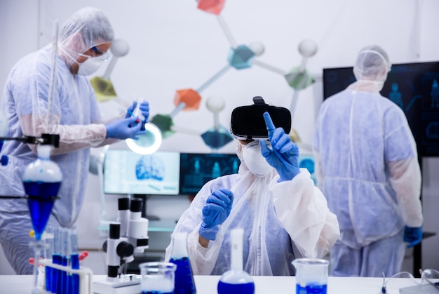 Female scientist pointing with finger wearing virtual reality goggles with her assistants in the background.