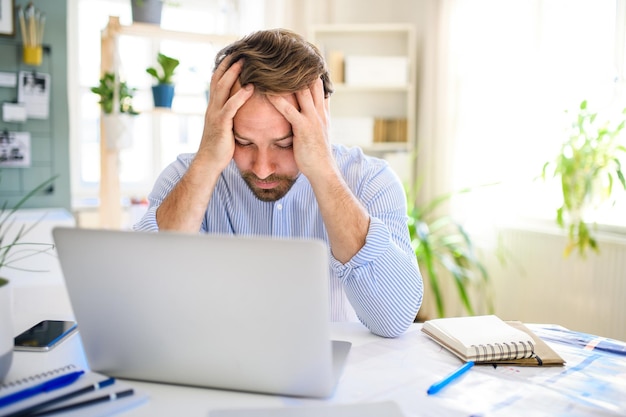 Frustrated mature businessman with laptop indoors in home office working