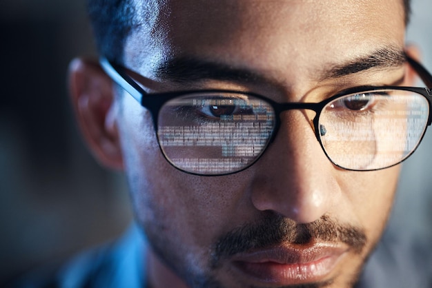 Glasses man and reflection of code on computer working on software programming and data IT engineer and serious face of developer with information technology for cyber security in office closeup