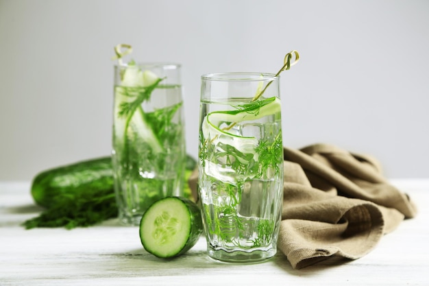 Glasses with fresh organic cucumber water on wooden table on grey background