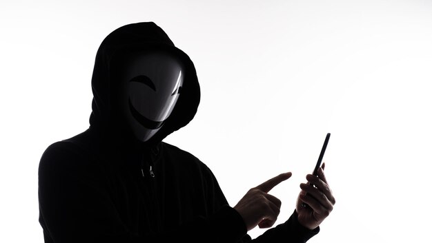 Hacker Anonymous and face mask with smartphone in hand
