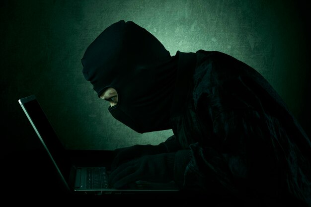 Hacker using laptop against wall