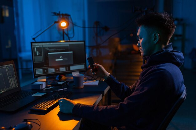 hacker with smartphone and computers in dark room
