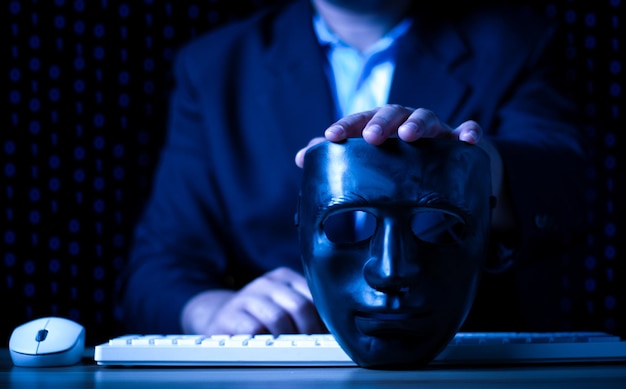 Hacking and malware concept Hacker using abstract laptop with binary code digital interface man holding a black mask