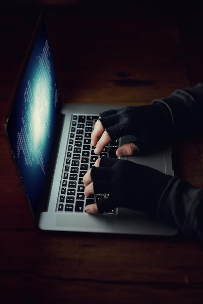 Hacking man and laptop screen for cyber attack at night crime software and typing for fraud Person programming malware and spam system or algorithm for phishing thief and coding script for info