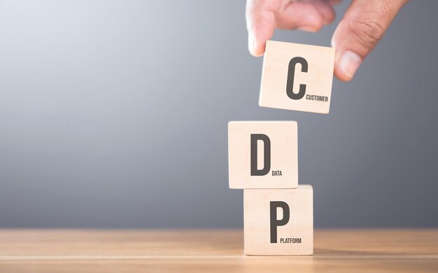 Hand arranging wooden blocks with the letters C D and P on a table Represents the concept of building a customer data platform emphasizing the importance of integrating these elements