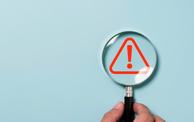 Hand holding magnifier glass with red triangle caution warning sign for focus notification error and maintenance concept