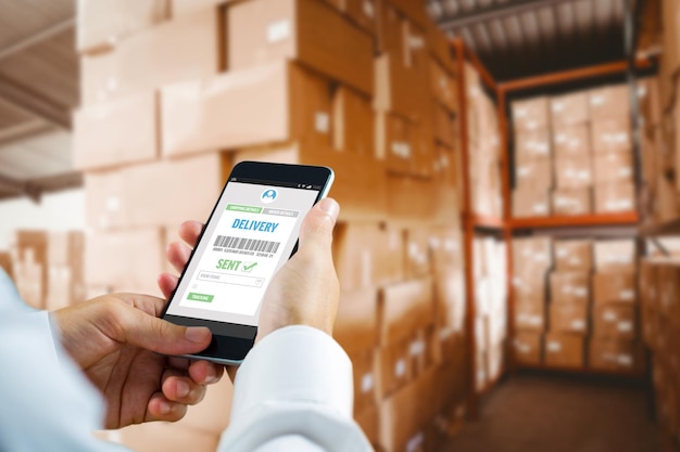 Hand holding smartphone against shelves with boxes in warehouse