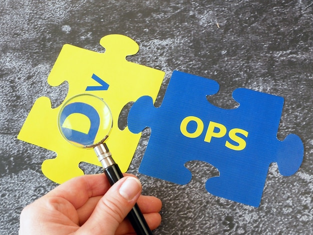 Hands with magnifier glass with words Dev and Ops puzzles