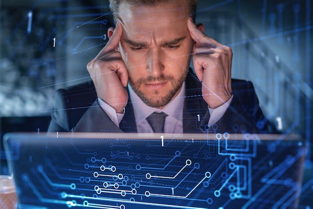Handsome businessman in suit at workplace working with laptop to optimize development by implying new technologies in business process Hi tech hologram over office background
