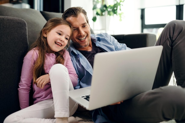 happy little girl and her father watching something on a computer while relaxing at home