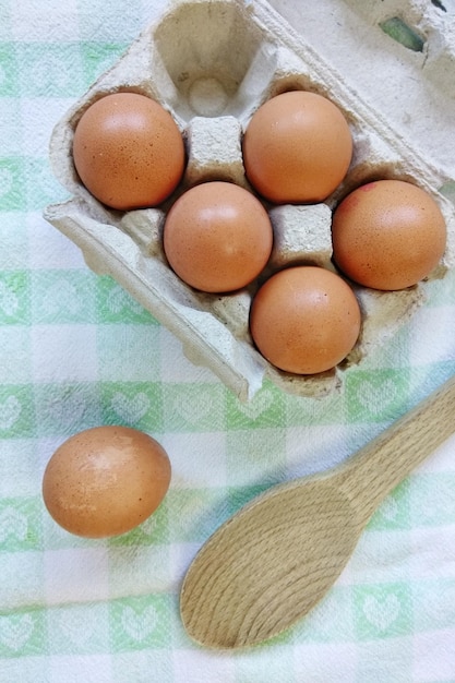 High angle view of brown eggs in carton by wooden spoon on table