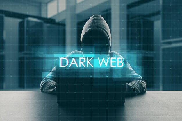 Internet crime concept with digital dark web sign on faceless hacker in hoodie in front of laptop background