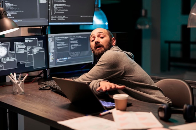 IT system engineer coding database on multiple monitors to program new server interface at night. Workign after hours to develop html source code on terminal window, artificial intelligence.