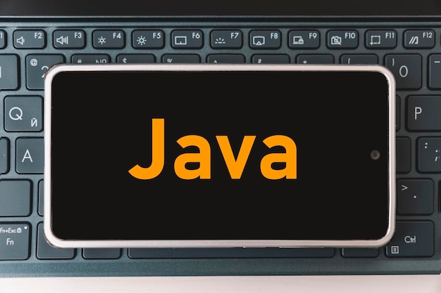 Java Programming language for mobile development concept Smartphone on the laptop keyboard the programmer workplace inscription java on mobile phone screen