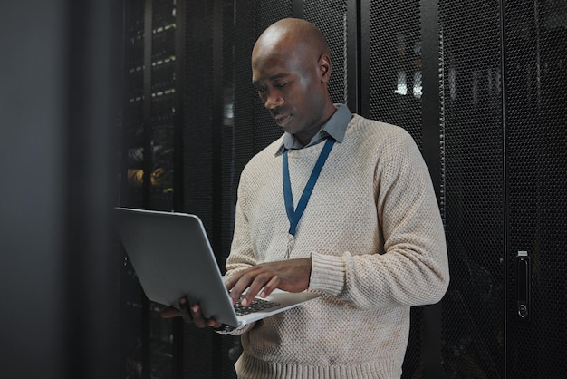 Laptop server room and black man or technician in data center management system or cybersecurity Analysis serious or power coding solution engineering programmer or information technology person