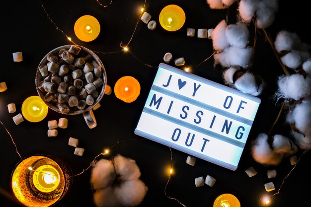 Lightbox with text JOMO Joy of Missing Out. The concept of relaxation from information and gadgets. Top view. Flat lay. Cup with cacao and marshmallows. Digital detox