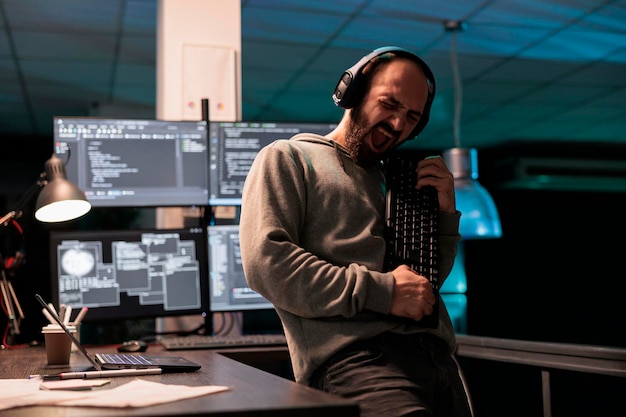 Male software engineer playing guitar with keyboard, writing code with cloud computing and programming html source. Cheerful smiling developer having fun and acting silly in office.