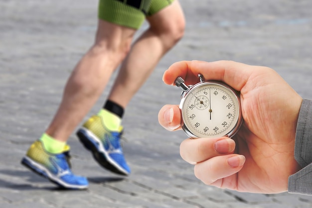 measuring the running speed of an athlete using a mechanical stopwatch hand with a stopwatch on the background of the legs of a runner