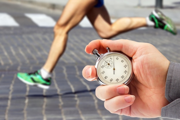 measuring the running speed of an athlete using a mechanical stopwatch hand with a stopwatch on the background of the legs of a runner