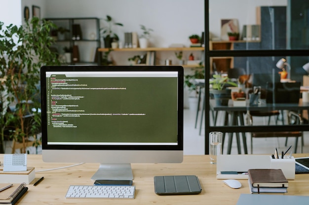 Medium close up of huge monitor with code lines and office supply on desk