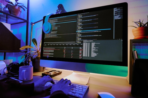 Medium close up of monitor with codes and headphones on desk unrecognizable male hands typing on