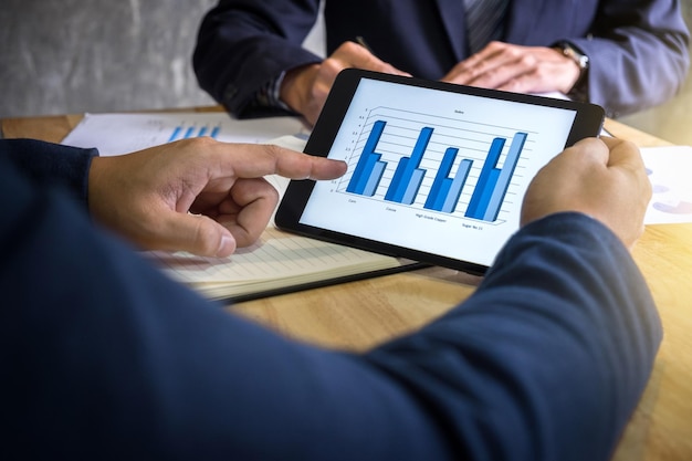Midsection of colleagues discussing graph on digital tablet in office