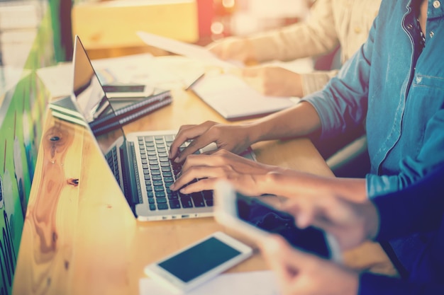 Midsection of colleagues using laptop and phone on table