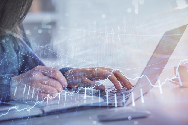 Näkymä, jossa liikenaisen kädet näkyvät kirjoittamassa tietokoneella ja forex-graafin hologrammi piirtää. Taloudellisen analyysin konsepti