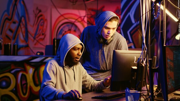 New member in hacking group receiving guidance from knowledgeable rogue programmer acting as his mentor in hidden base African american hacker teaches script kiddie how to hack computers