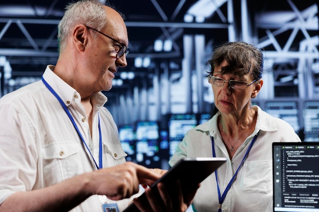 Old cloud computing business executives updating server clusters writing intricate binary code scripts on tablet and laptop using programming to fortify cybersecurity in high tech workplace