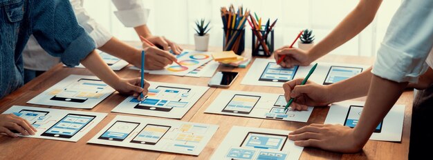 Panorama shot of frontend developer team brainstorming UI and UX designs for mobile app on paper wireframe interface User interface development team planning for userfriendly UI design Scrutinize
