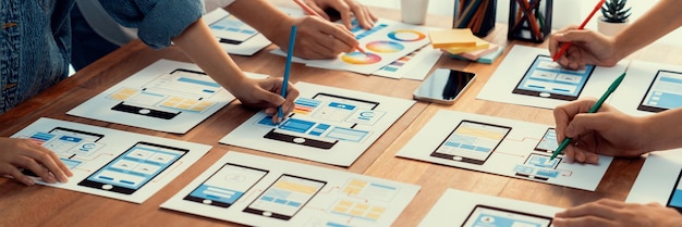Panorama shot of frontend developer team brainstorming UI and UX designs for mobile app on paper wireframe interface User interface development team planning for userfriendly UI design Scrutinize