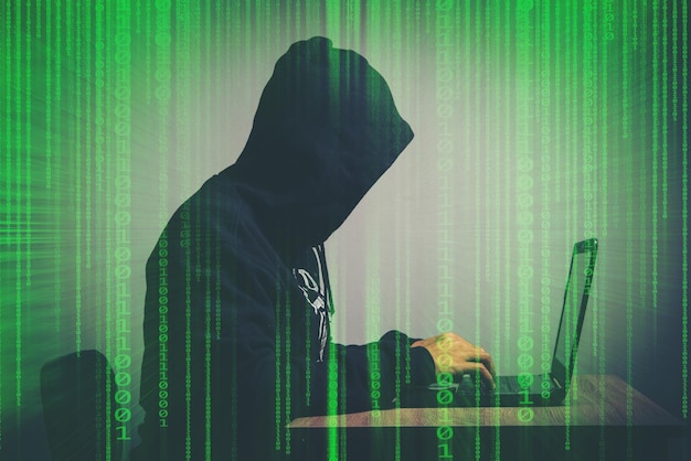 Person wearing hood while using laptop on table over gray background