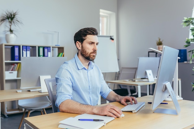 Portrait of a serious and focused businessman a man working in a bright office during the day at the computer looking at the monitor in casual clothes