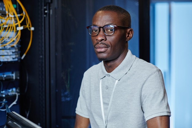 Portrait of black adult man working as it engineer in server room and looking at camera copy space