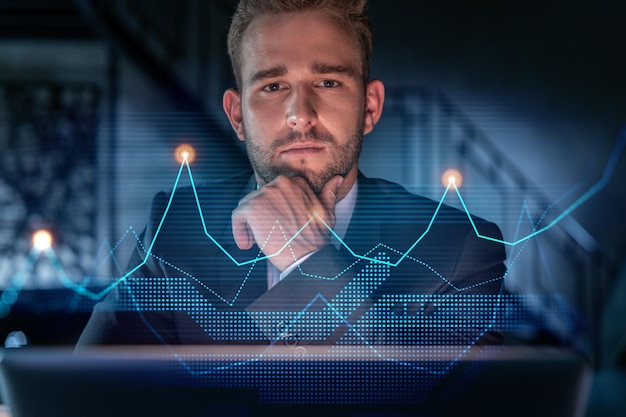Portrait of handsome businessman in formal suit thinking how to optimize trading strategy at corporate finance fund Forex chart hologram over modern office background Hand on chin