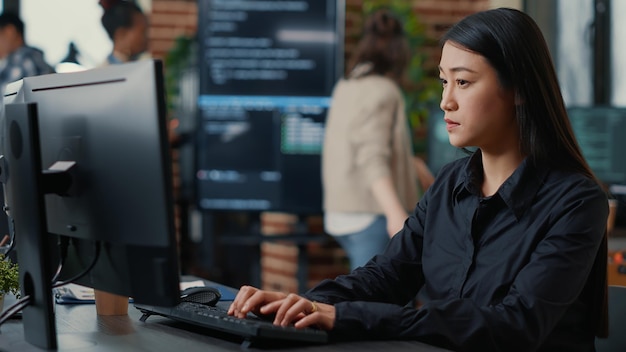Programer writing algorithm focused on compiling source code sitting at desk in software development office with team working in background. Concentrated system engineer working on parsing data.