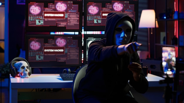 Scammer with anonymous mask using cellphone to record blackmail footage threatening victims