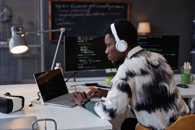 serious programmer in wireless headphones developing new program on computer while working in it office