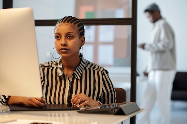 Serious young black woman looking at computer screen while drawing
