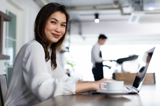 Smiling Business girl working with laptop. Happy Asian business woman using computer at coffee cafe. young people with laptop Contact for work. Concept working in coffee cafe.