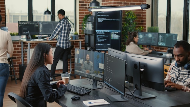 Software company employee in video call conference with business owner discussing coding project deadline in office with team working. Programer having online chat with client about source code.