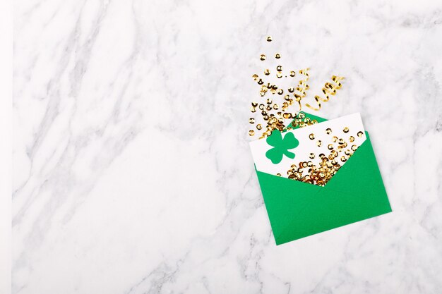 st. patrick's day concept. empty card with green envelope and gold confett and clover leafi. mockup template. view from above