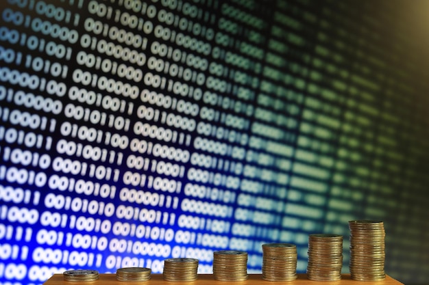 Stacked coins against binary code on screen