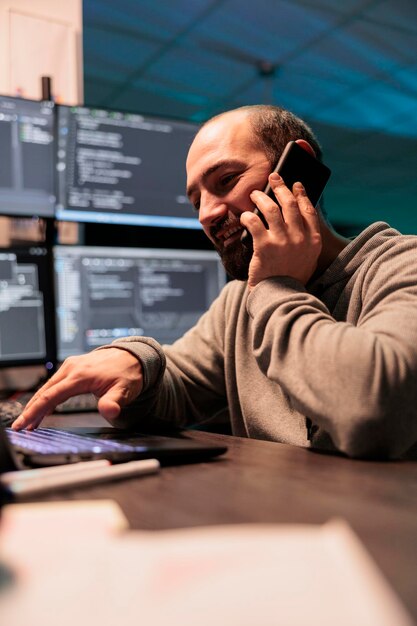 System engineer answering phone call late at night, talking to coders on smartphone and programming html script. Chatting on mobile phone and developing new it source code.