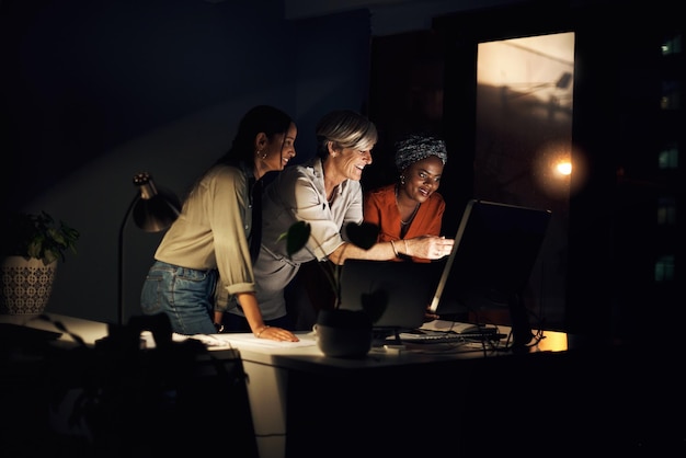 Teamwork women and computer at night for project research or together in creative agency Collaboration designers and online in office for brainstorming review and planning or support in company