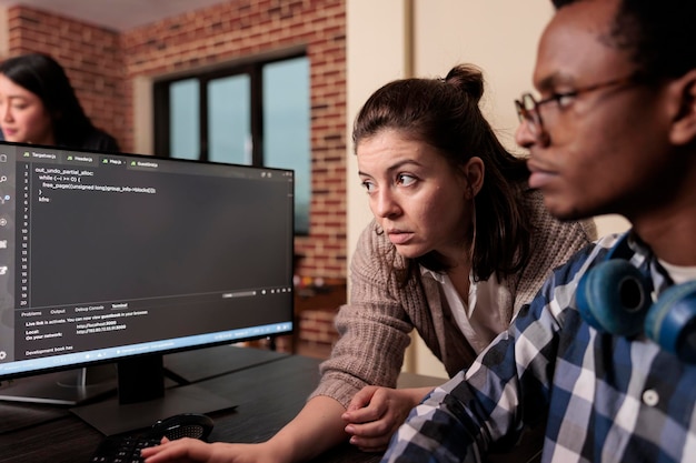 Tech enginner asking app designer for help with html code, pointing at database script on terminal window. Team of programming engineers working on app developing program in it agency.