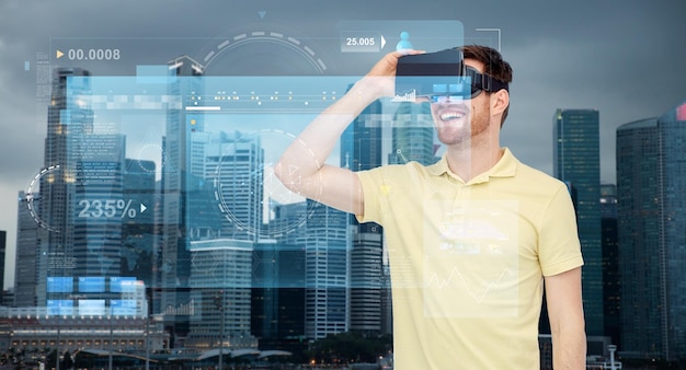 technology, augmented reality, entertainment and people concept - happy young man with virtual headset or 3d glasses over singapore city skyscrapers background and screens projection
