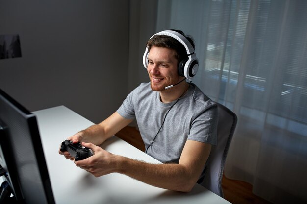 technology, gaming, entertainment, let&amp;#39;s play and people concept - happy young man in headset with controller gamepad playing computer game at home and streaming playthrough or walkthrough vid
